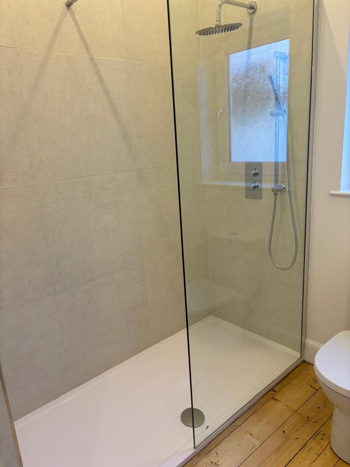 Walk-in glass shower enclosure with herringbone floor tiling